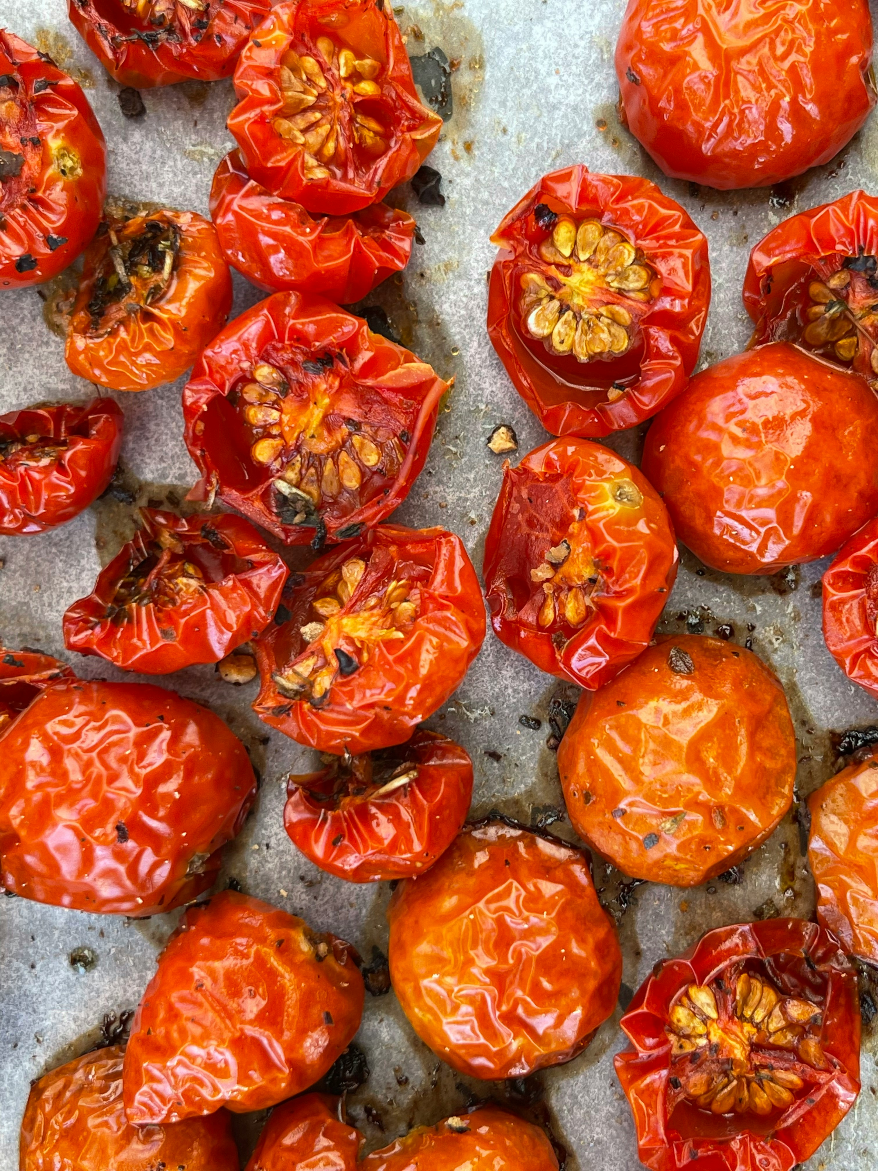 Semi-dried sunblush tomatoes on a baking tray, slow-roasted until wrinkled, glossy and lightly caramelised.